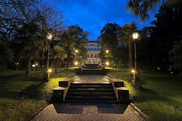 Vista nocturna del complejo termal de Tskaltubo iluminado entre palmeras y senderos de jardín en Georgia